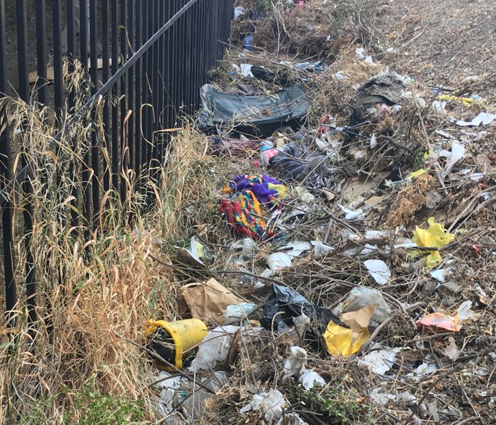 trash along a fence by homeless encampment