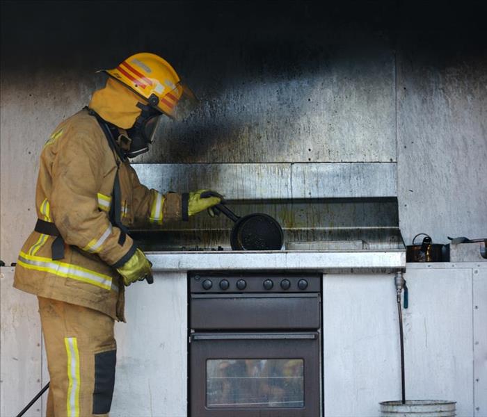 Fire fighter standing by a soot covered stove.